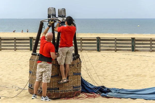 Двое мужчин проверяют корзину с воздушным шаром на песке — стоковое фото