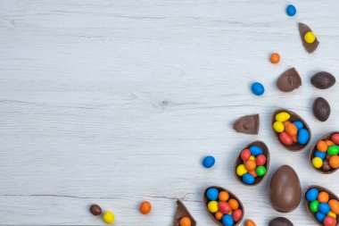 Çikolatalı Paskalya yumurtaları ve çikolatalı yumurtalar beyaz ahşap masada tatlı ve renkli şekerlerle dolu. Boşluğu kopyala, üst görünüm.