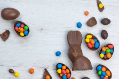 Çikolatalı tavşan ve yumurtalar beyaz ahşap masanın üzerinde tatlı ve renkli şekerlerle dolu. Boşluğu kopyala, üst görünüm.