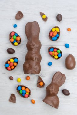 Çikolatalı tavşan ve yumurtalar beyaz ahşap masanın üzerinde tatlı ve renkli şekerlerle dolu. Üst görünüm.