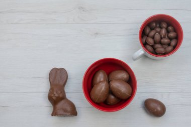 Lezzetli çikolatalı Paskalya tavşanı ve seramik kaselerde yumurtalar. Beyaz ahşap arkaplan, üst manzara.