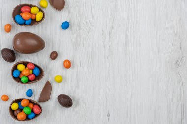 Çikolatalı Paskalya yumurtaları ve çikolatalı yumurtalar beyaz ahşap masada tatlı ve renkli şekerlerle dolu. Boşluğu kopyala, üst görünüm.