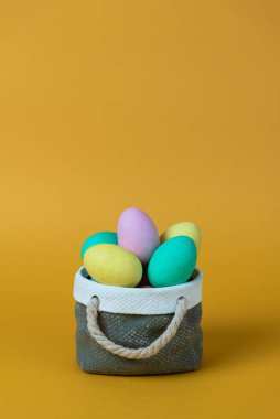 Seramik sepet konseptli renkli paskalya yumurtaları. Kopyalama alanı ve turuncu arkaplan ile görüntüle.