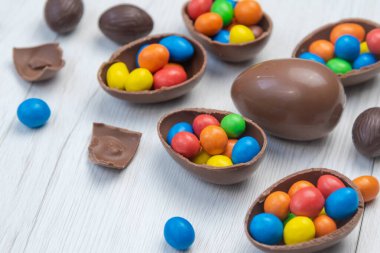 Çikolatalı Paskalya yumurtaları ve çikolatalı yumurtalar beyaz ahşap masada tatlı ve renkli şekerlerle dolu. Kapat..