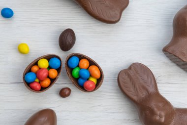 Çikolatalı tavşan ve yumurtalar beyaz ahşap masanın üzerinde tatlı ve renkli şekerlerle dolu. Üst görünüm.