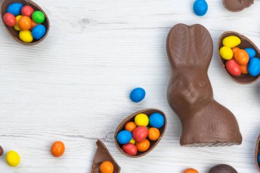 Çikolatalı tavşan ve yumurtalar beyaz ahşap masanın üzerinde tatlı ve renkli şekerlerle dolu. Boşluğu kopyala, üst görünüm.