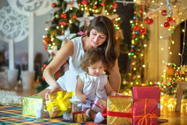 Hamile anne ve küçük kızı, birlikte şenlikli bir köknar ağacı yakınındaki bir katta oturmak, oynamak ve hediyeler göz önünde bulundurun. Bir tatil bekliyor.