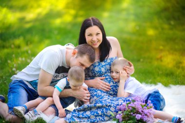 parkta yürüyüş mutlu aile, bir çim üzerinde oturan kucaklamak ve eğlenmek