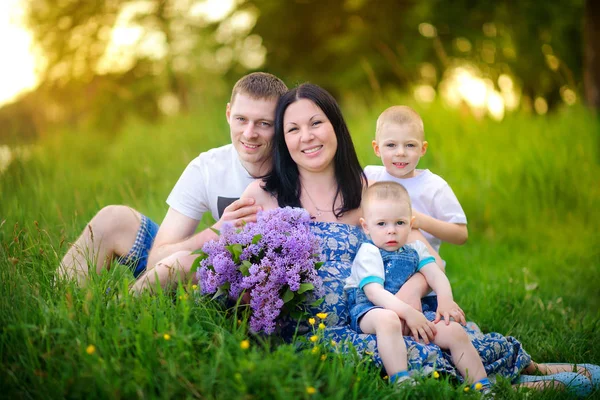 gün batımında parkta yürümek mutlu aile, bir çim üzerinde oturup kucaklamak