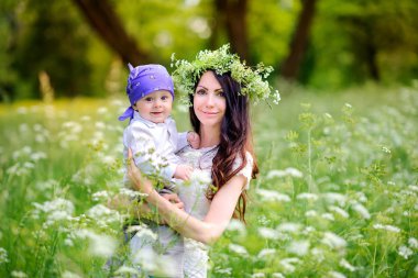 anne bir gün batımında güzel parkta çocuklarla yürür, güçlü kucaklar ve ellerde tutar. Başındaki annenin yabani çiçeklerden çelenk var.
