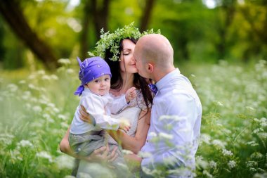 güzel bir gün batımı parkta çocuklar ile genç aile yürür, dostça kucaklamak ve öpmek, anne baş vardır kır çiçekleri gelen bir çelenk