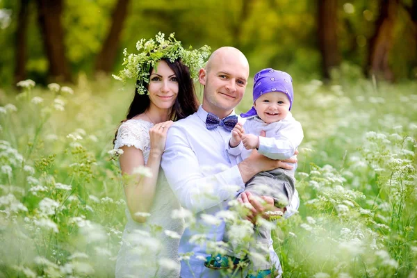 güzel bir gün batımı parkta çocuklar ile genç aile yürür, dostça kucaklama ve gülümseme, anne baş vardır kır çiçekleri gelen bir çelenk