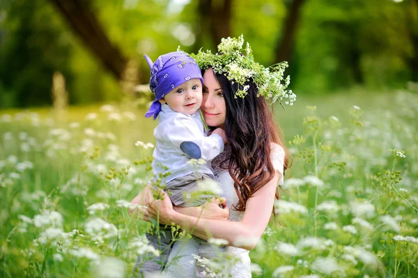 anne bir gün batımında güzel parkta çocuklarla yürür, güçlü kucaklar ve ellerde tutar. Başındaki annenin yabani çiçeklerden çelenk var.