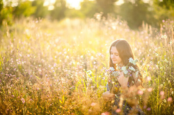 Happy girl walking in a field with a big bouquet, at sunset sun