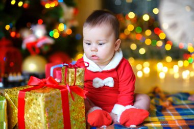 mutlu bir çocukluk Noel Baba kostüm hediyeler, arka plan parlak Festival ışık yanında yerde yatıyor