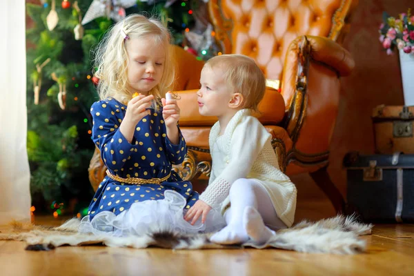 两个小女孩一起玩口红坐在地板上 在背景一棵喜庆的圣诞树 — 图库照片