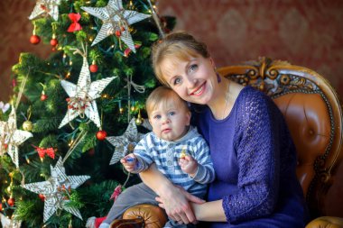 şenlikli bir Noel ağacının yanında oturan bebek ile mutlu anne