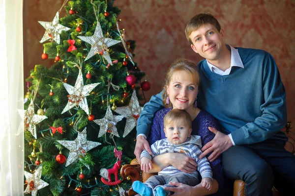 お祝いクリスマス ツリーのそばに座って赤ちゃんと幸せな家庭 — ストック写真