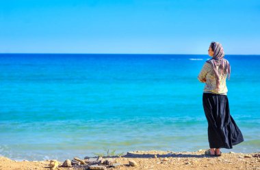 Kafasındaki bir Fularlı güzel bir kız sahilde duran ve bir şey hakkında hayal