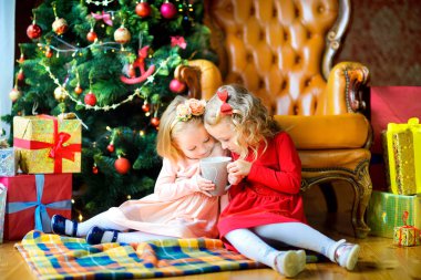 iki güzel kız zarif elbiseler şenlikli Noel ağacı yakınındaki katta oturan ve sıcak te içme