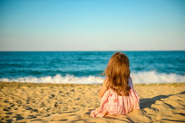 Klein Meisje Een Jurk Zittend Het Strand Dromerig Kijken Naar — Stockfoto