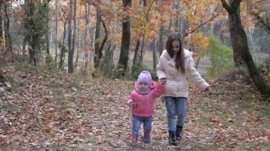 bir kız güzel bir parkta küçük kız kardeşi ile yürüyor, elini tutar ve onu yürümeyi öğretiyor