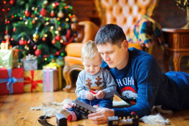 Sevgili oğlu, neşeli Noel ağaçları ve hediye kutuları ile oynarken yerde yatan baba