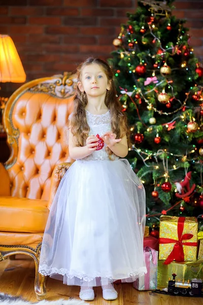 ドレスの少女はボールお祝いクリスマス ツリーを飾ります — ストック写真
