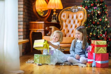 güzel kız yılbaşı ağacı yakınındaki katta oturmak ve mevcut birbirlerine vermek