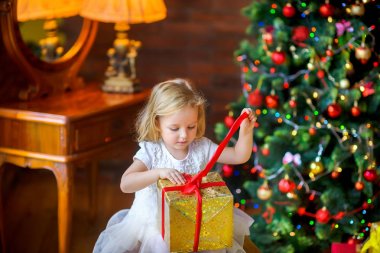 Festival elbiseli güzel küçük kız bir Noel tre oturan bir hediye açar