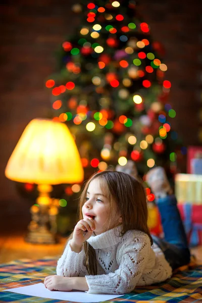 güzel kız yerde Noel tre arka plan şenlikli ışıkları yalan Noel Baba'ya bir mektup yazar