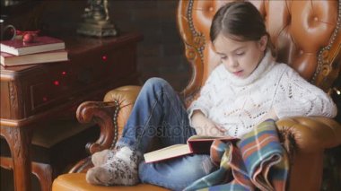 bir kız bir örme beyaz kazaklı bir sandalyede elverişli bir konumdadır ve masal okur