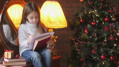 Beyaz örgü kazak, güzel küçük bir kız yere yatıyor, oluşturur ve şenlikli bir Noel ağacı ve hediyeler bir dizi arka planda Noel Baba'ya bir mektup yazar