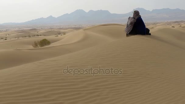 孤独な少女が砂漠の砂丘の上に座って夢を見ている — ストック動画