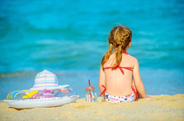 küçük bir kız sahil üzerinde oturur ve yüzme ve plaj şapka şişme bir daire yalan yanında mesafe içine bakıyor