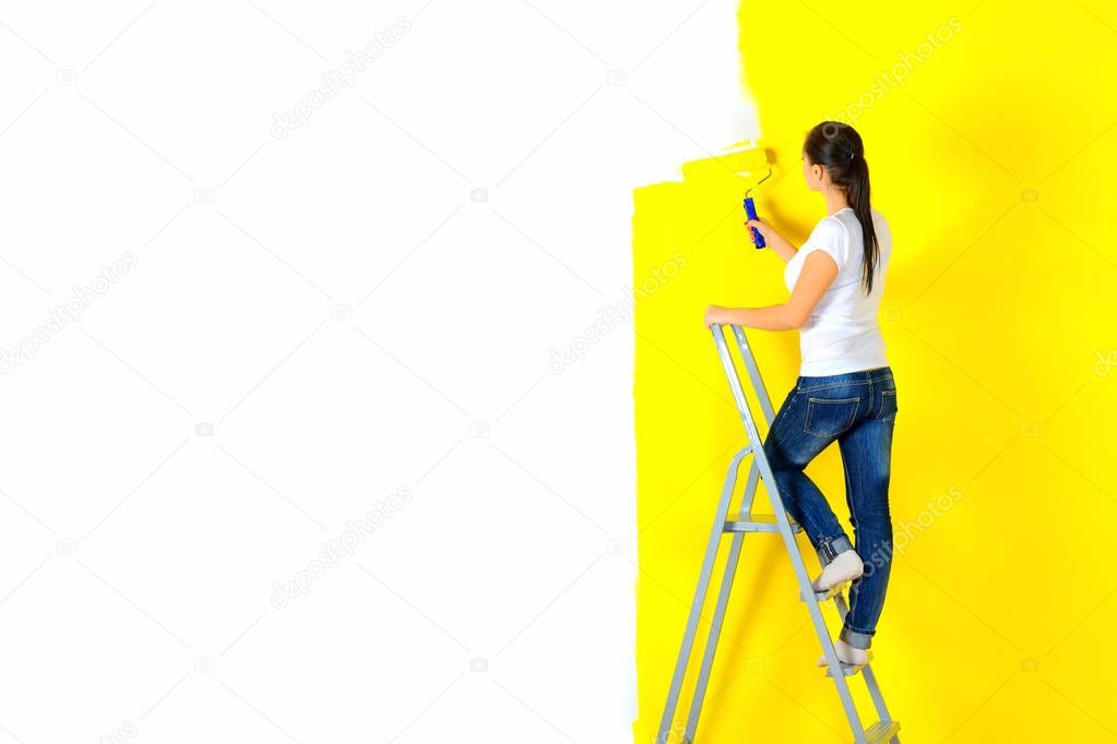 girl painter paints a wall with a platen standing on a staircase