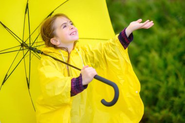 Cute little girl in a raincoat and with an umbrella in her hands walks outdoors