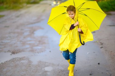 Cute little girl in a raincoat and with an umbrella in her hands walks through puddles