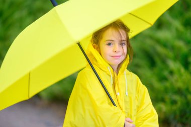 Cute little girl in a raincoat and with an umbrella in her hands walks outdoors