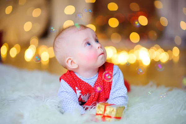 面白い子供は小さなギフトボックスと床の上にあり 明るいお祝いの光の中で驚きを見ています クリスマスプレゼント — ストック写真