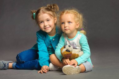 Sade gri bir arka planda yerde oturan iki tatlı kızın portresi.