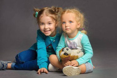 Sade gri bir arka planda yerde oturan iki tatlı kızın portresi.