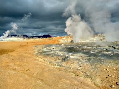 İzlanda. Turistler türmal kaynakların etrafında yürürler. Sıcak pınarların üzerinden buhar yükseliyor..