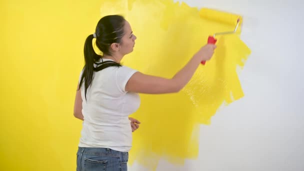 The girl makes repairs in the room. Woman paints a wall with a roller in yellow. Repair in the room. Renewal. — Stock Footage Girl Makes Repairs Room Woman Paints Wall Roller Yellow Repair Royalty Free Stock Footage