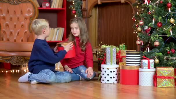 Kinder Beschenken Sich Auf Dem Boden Neben Dem Weihnachtsbaum Sitzend — Stockvideo