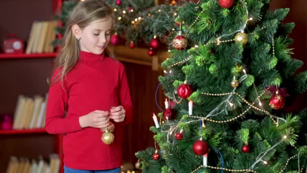 Schattig Meisje Een Rode Trui Versiert Kerstboom Kamer Met Decoratieve — Stockvideo