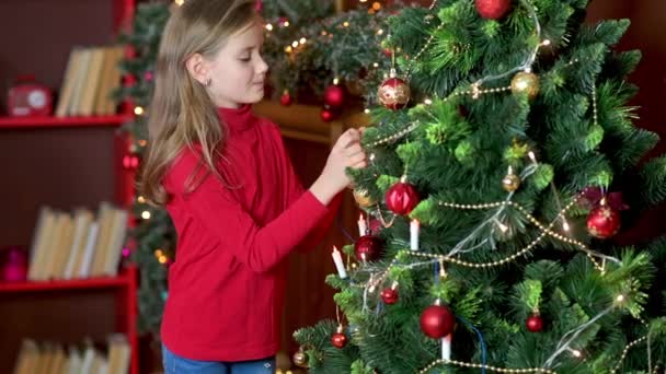 Nettes Mädchen Roten Pullover Schmückt Den Weihnachtsbaum Zimmer Mit Dekorativen — Stockvideo