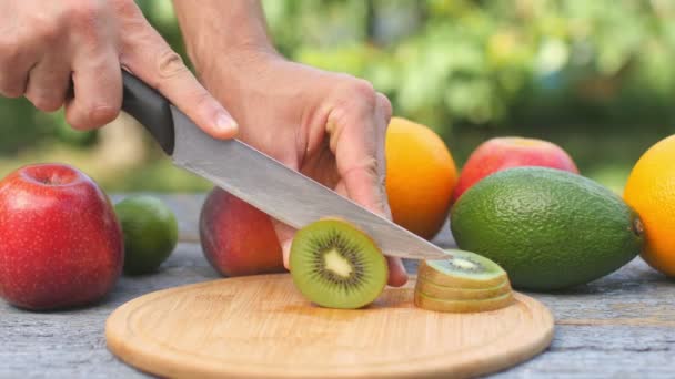 雄的手把成熟多汁的猕猴桃切成薄片 各种水果躺在一张木制桌子上 健康食品 在绿色的自然背景上 Uhd — 图库视频影像
