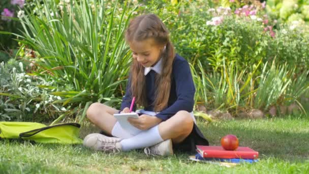 Schule Schulmädchen Sitzt Auf Dem Gras Und Schreibt Ins Notizbuch — Stockvideo