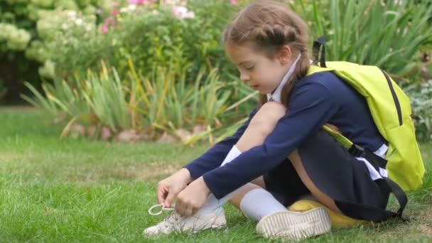 バックパックを持った女子高生が芝生に座り 靴ひもを結ぶことを学ぶ 学校の準備 — ストック動画